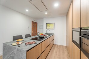 Een moderne keuken met een marmeren aanrechtblad, houten kastjes, een ingebouwde oven en een eethoek met stoelen.