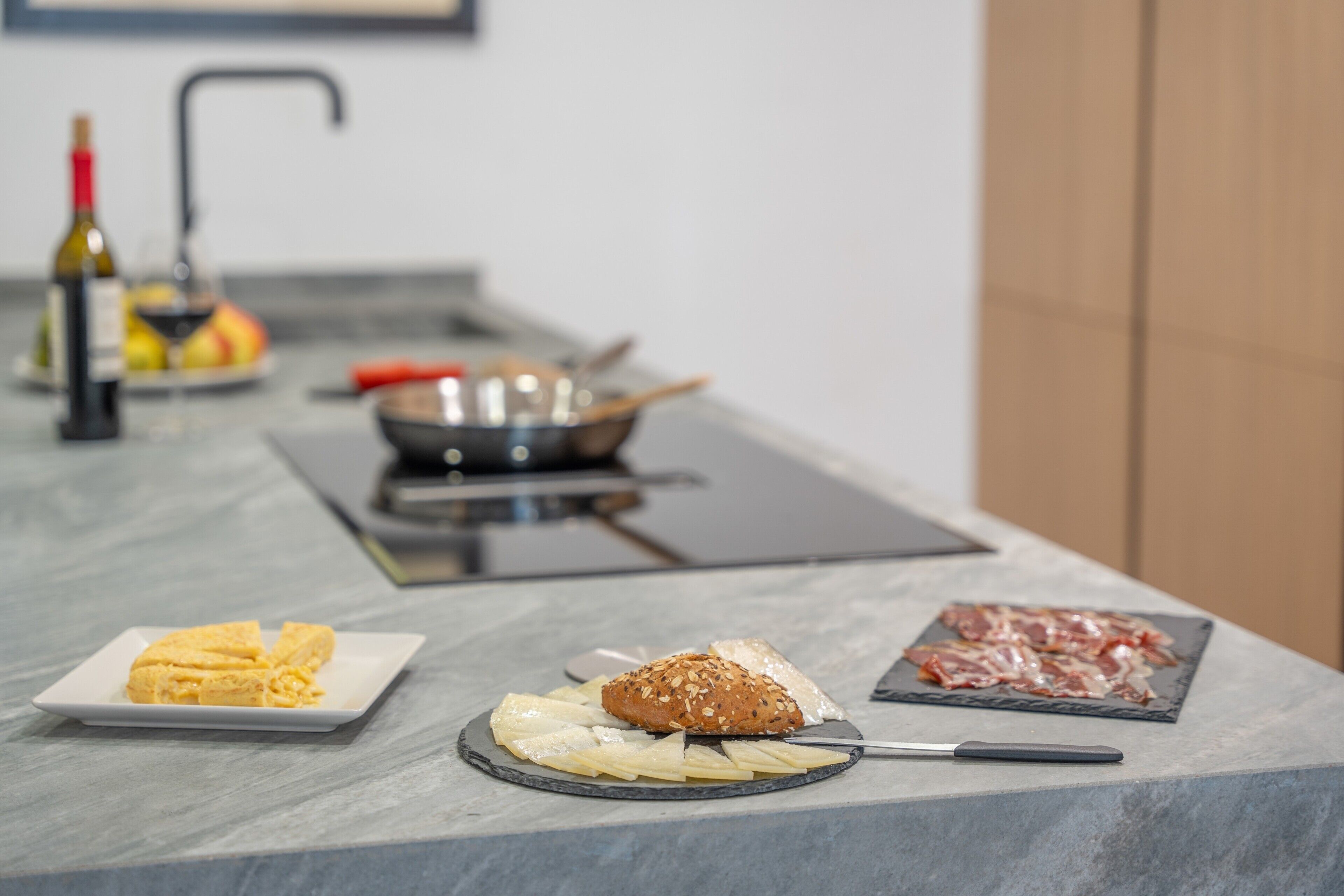 Een keukentafel met een snijplank, een mes, een brood, een bord kaas en een bord vlees.