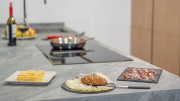 Een keukentafel met een snijplank, een mes, een brood, een bord kaas en een bord vlees.