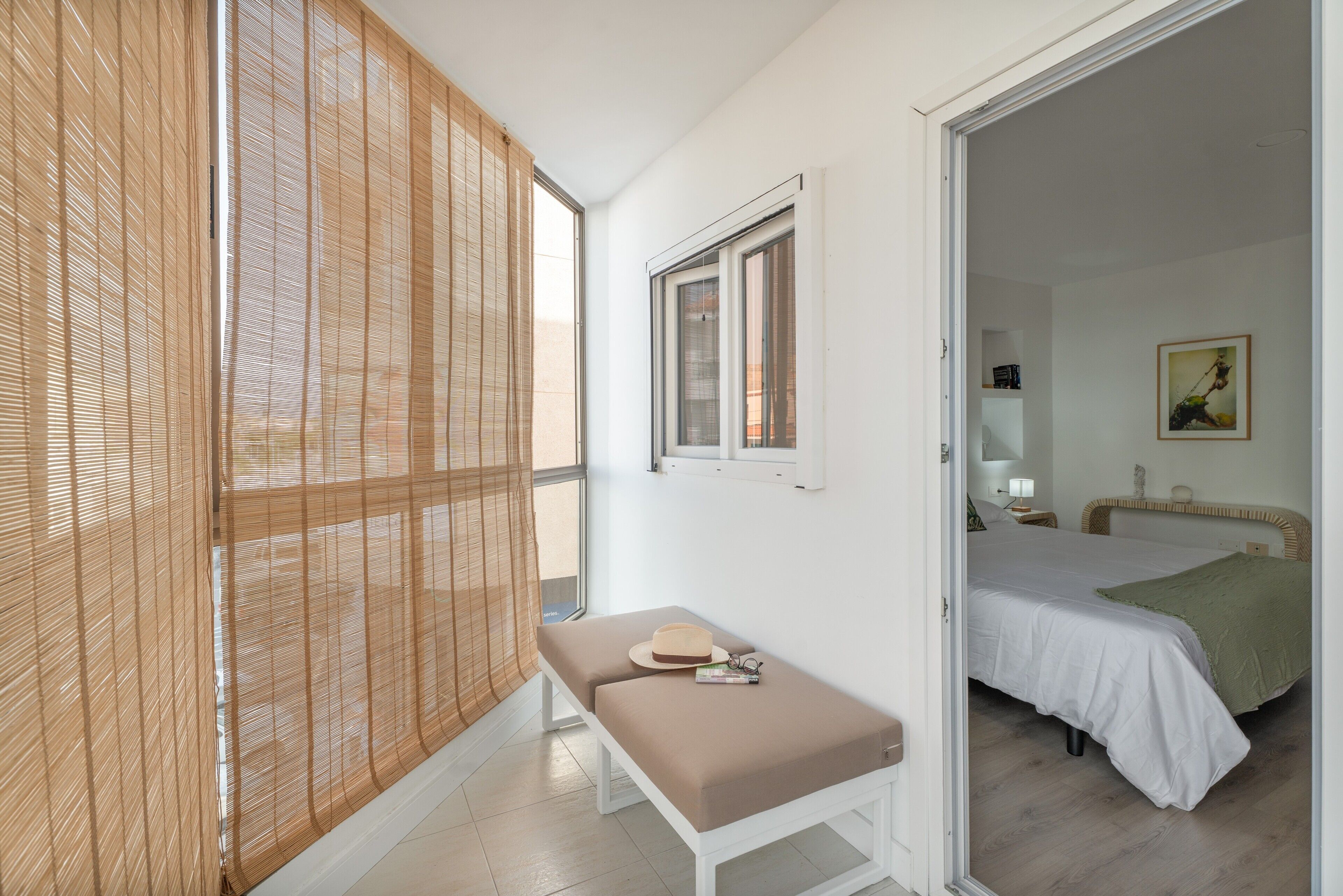 Een kamer met een bed, een bankje, een raam en een deur naar een andere kamer.