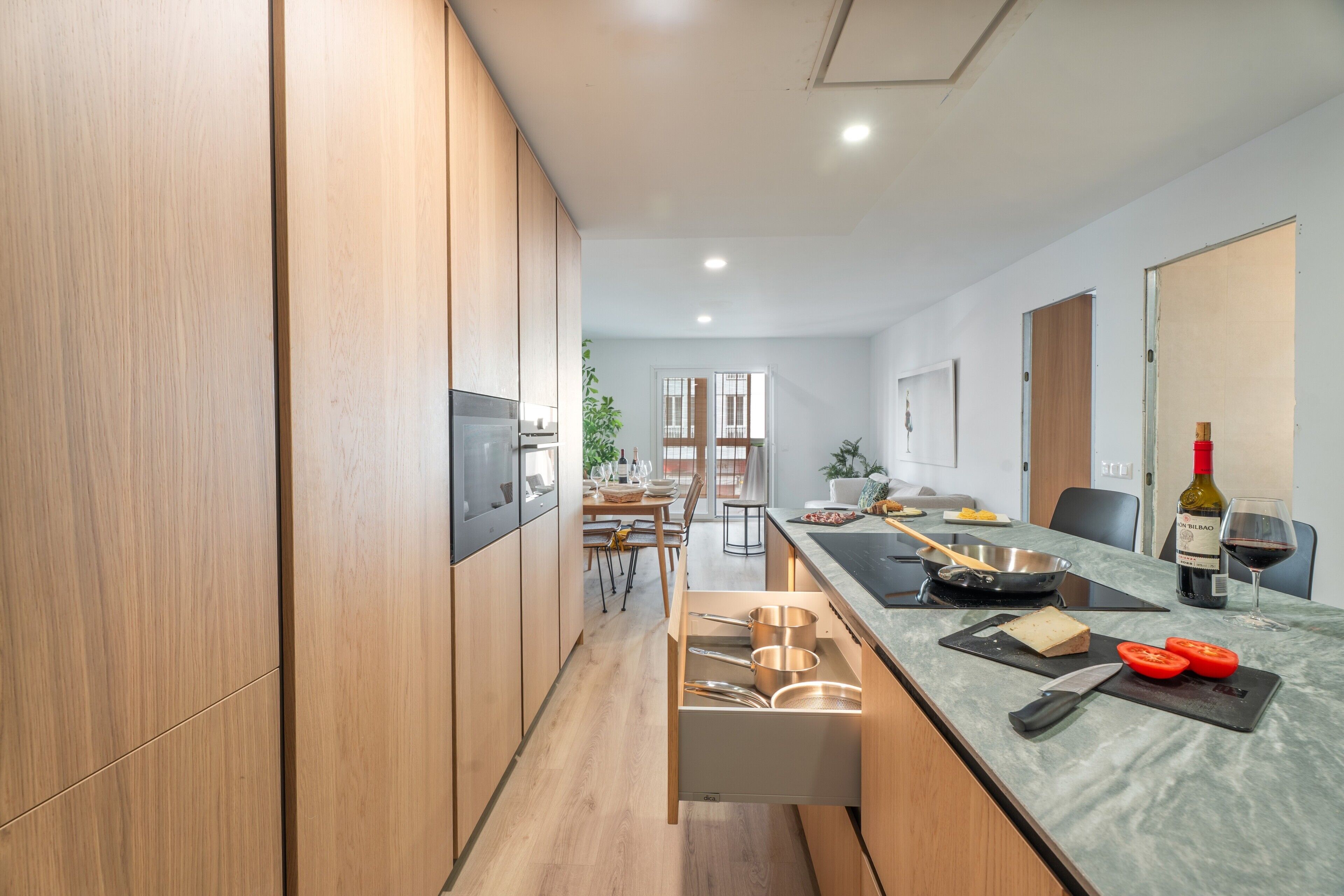 Eine moderne Küche mit Holzausstattung, einem Essbereich mit Tisch für Zwei und einer Weinflasche auf der Arbeitsplatte.
