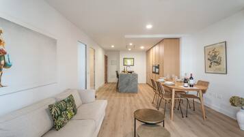 A modern living room with a sofa, a dining area with a table and chairs, and a kitchen in the background.