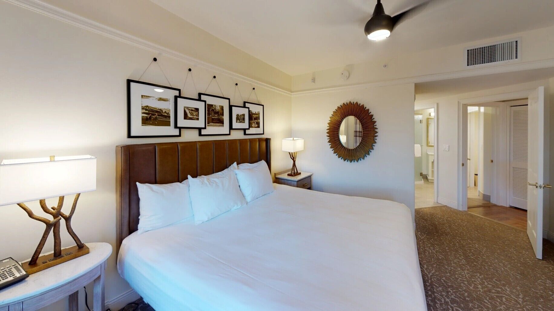 Habitación de hotel con una cama grande, una mesita de noche con lámpara, cuadros en la pared y un espejo.