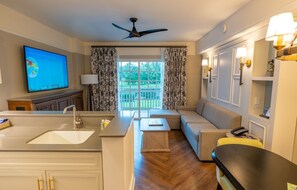 Ein modernes Hotelzimmer mit Küchenzeile, einer Sitzecke mit Sofa und Sesseln, einem Flachbildfernseher und einem Balkon mit Vorhängen.