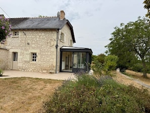 A stone house with a modern glass extension, a paved driveway, and surrounding vegetation.