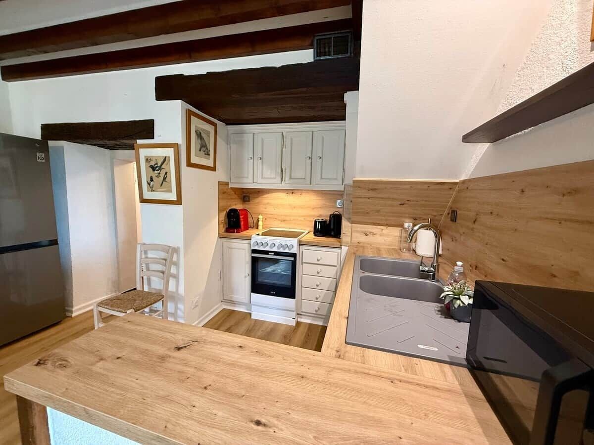 A compact kitchen with white cabinets, a built-in oven, a sink, and a wooden countertop.