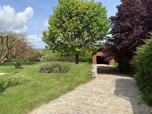 A paved pathway leading to a wooden structure, surrounded by lush greenery and trees.