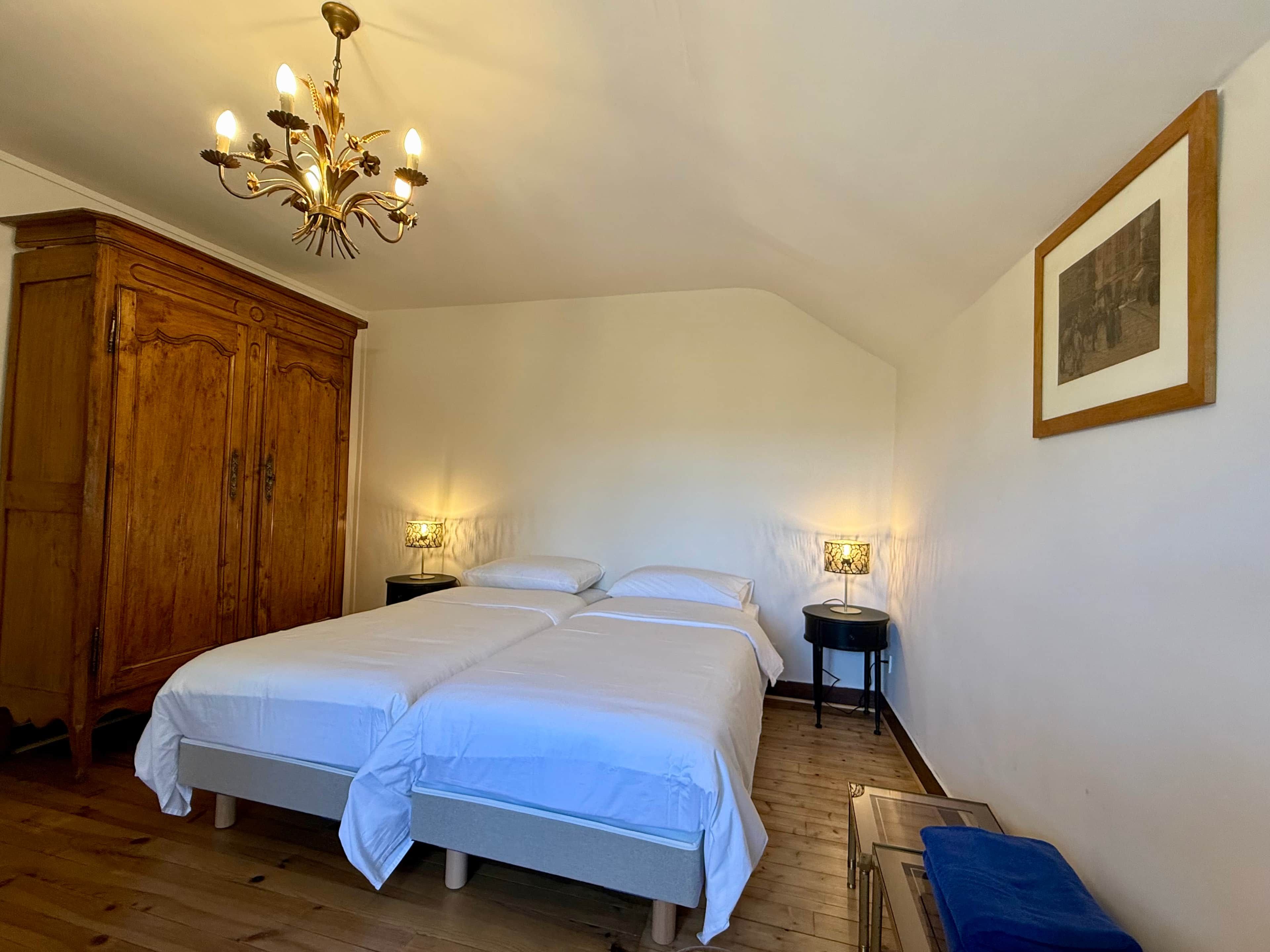 A double bed with two bedside tables, a wooden wardrobe, and a chandelier.