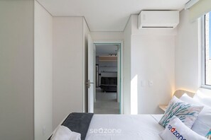 Ein Schlafzimmer mit Bett, Kissen, Nachttisch, Fenster und Klimaanlage.