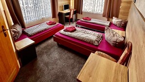 A compact room with two beds, a desk, and a chair.