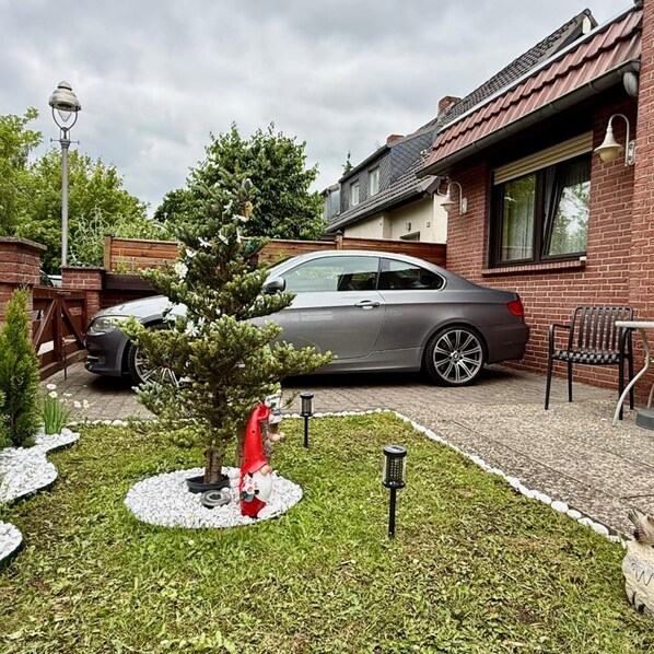 A residential driveway with a parked car, a small garden with a decorative tree, and a brick house. - Hotel Pension Pamina (Berlin)