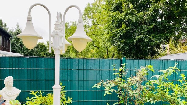 A garden with a white lamp post, a bench, and a small table with a decorative item.