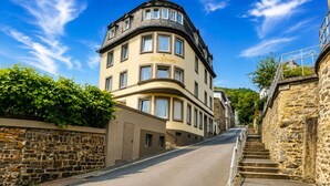 Uma rua que leva a um edifício com fachada curva e uma parede de pedra de um lado.
