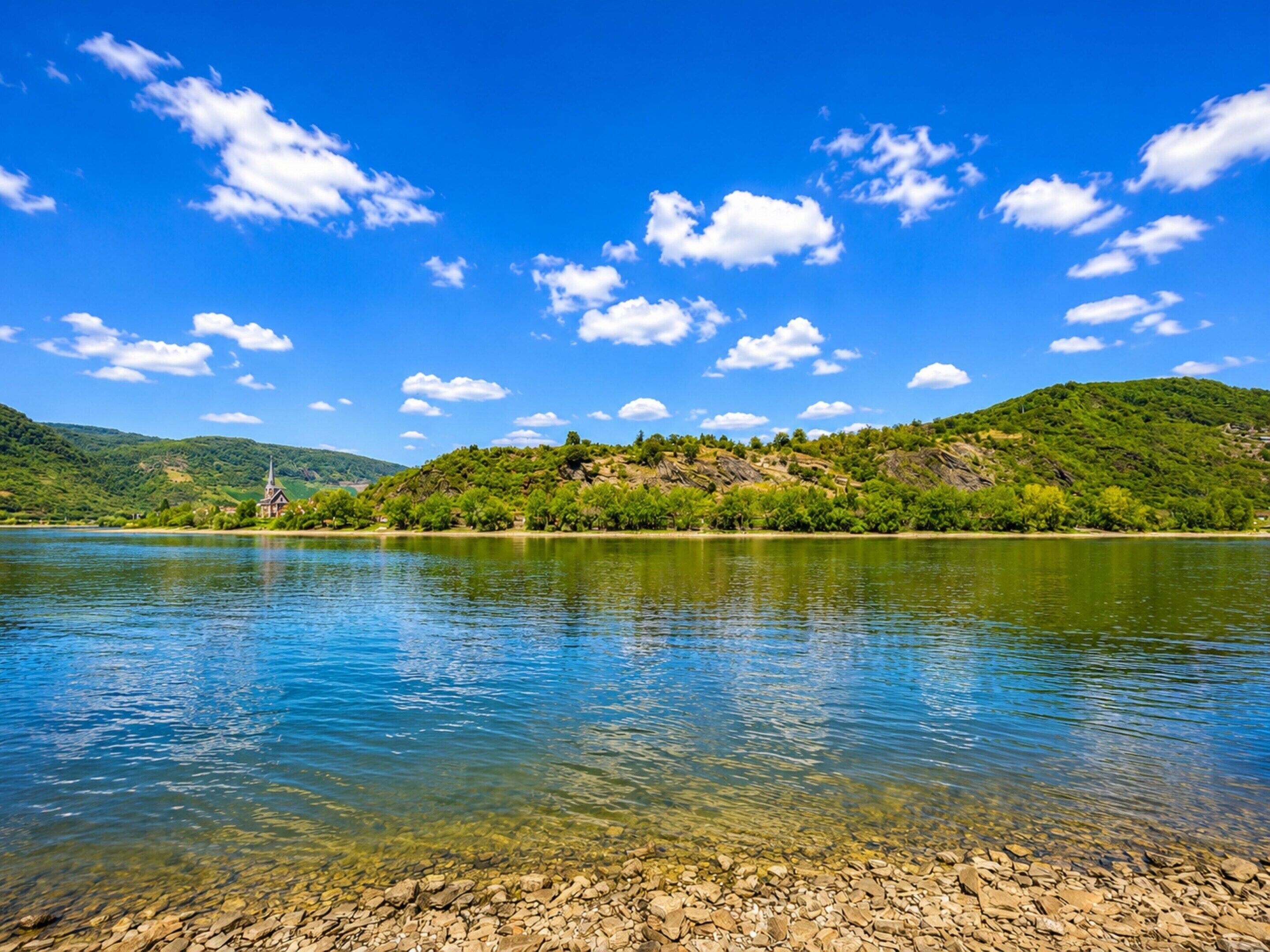 A clear lake with a church on a hill, surrounded by greenery.