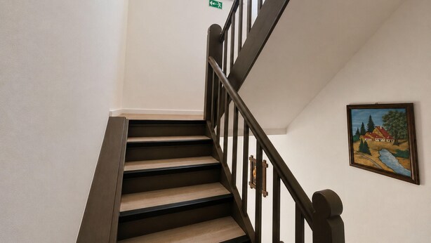 Eine Treppe mit Holzbeschlägen und dunklen Geländern, ein kleines Fenster mit Pflanze und ein gerahmtes Landschaftsbild an der Wand.