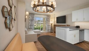 Ein modernes Wohnzimmer mit einer Couch, einer Bank, einem Essbereich mit Küche und einem großen Fenster mit Vorhängen.