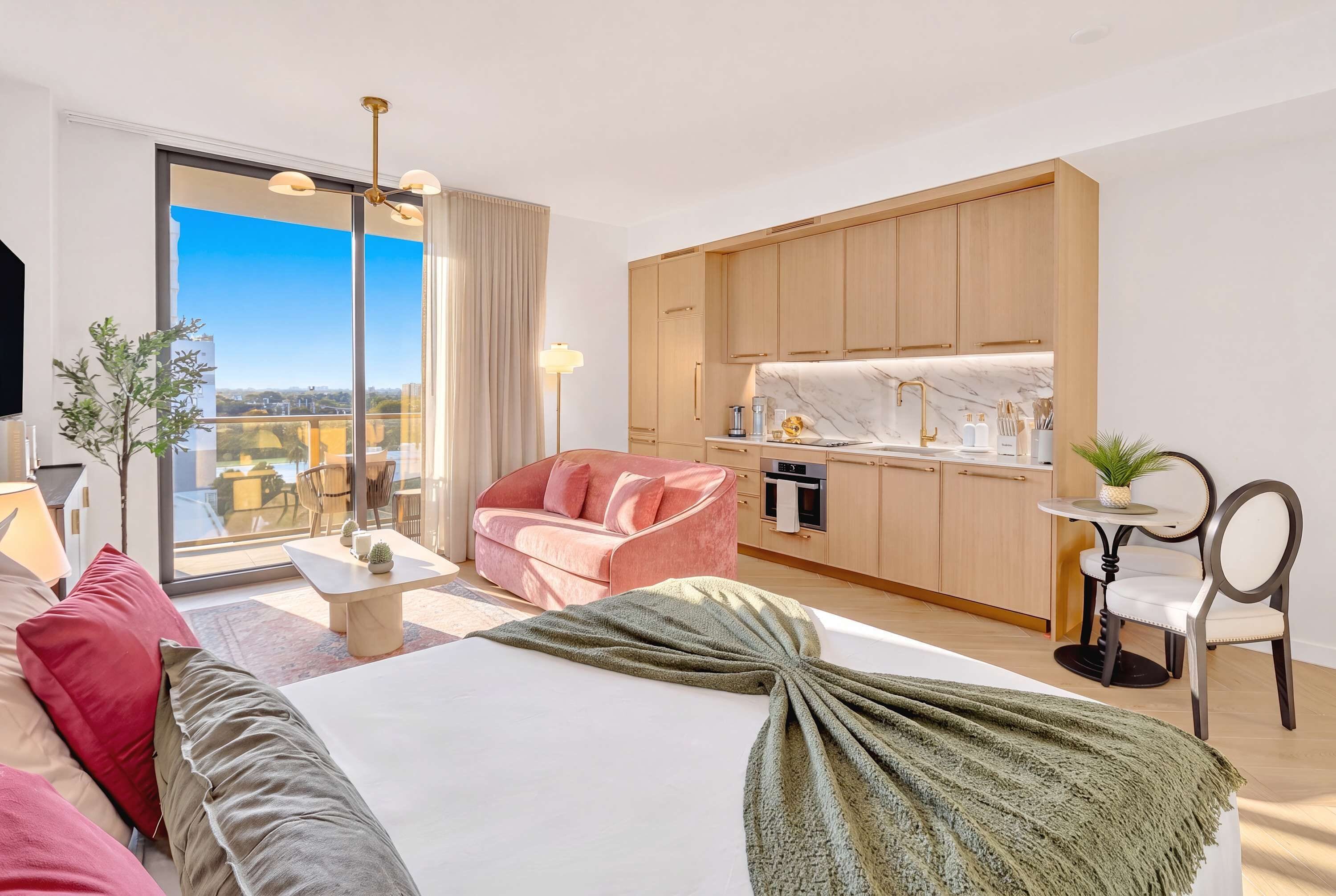 Ein modernes Hotelzimmer mit Bett, Sitzecke, einer Küchenzeile und einem Balkon mit Blick auf die Stadt.