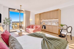 A modern hotel room with a bed, a seating area, a kitchenette, and a balcony with a city view. - Luxury Wynwood Studio with Pool, Gym & NoMad Bar (Miami)