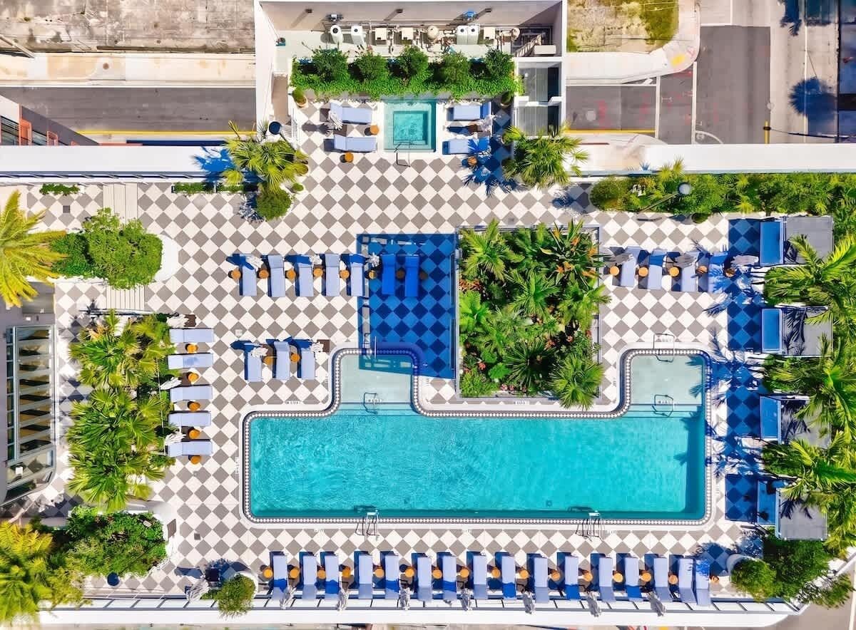 Luftaufnahme eines Hotelpoolbereichs mit mehreren Pools, Liegestühlen und viel Grün.