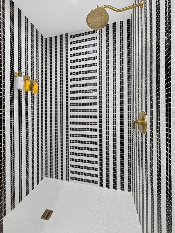 A bathroom with a black and white striped tile wall, a gold showerhead, and two wall-mounted light fixtures. - Luxury Wynwood Studio with Pool, Gym & NoMad Bar (Miami)