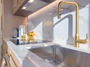 Eine moderne Küche mit einer Edelstahl-Spüle, einem Wasserhahn aus Gold und einer Marmor-Spritzschutzwand.