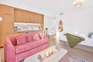 Ein modernes Wohnzimmer mit einem rosa Sofa, einem Couchtisch mit Kerzen und einer grünen Decke auf einem Bett.
