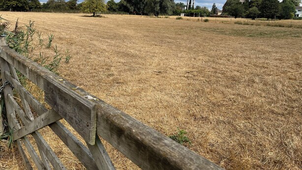A dry grass field with a wooden fence in the foreground and a water tower in the background. - Laurel (Wisbech)
