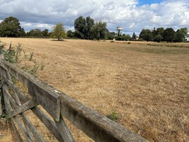 Campo de hierba seca con una cerca de madera en primer plano y un torre de agua al fondo.