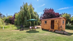 A wooden cabin with a door open, a table with chairs, and a green umbrella. - Laurel (Wisbech)