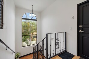 Eine Treppe mit schwarzem Geländer, eine Tür mit einer Nummer und ein Fenster mit Blick auf Palmen.