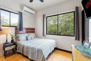 Ein Hotelzimmer mit Bett, Schreibtisch, Klimaanlage, einem Fenster mit Vorhängen und Blick auf Bäume.
