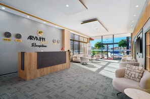 A reception area with a wooden desk, seating, and a wall with clocks and city names. - ARYA INN SUİT  (Serik)