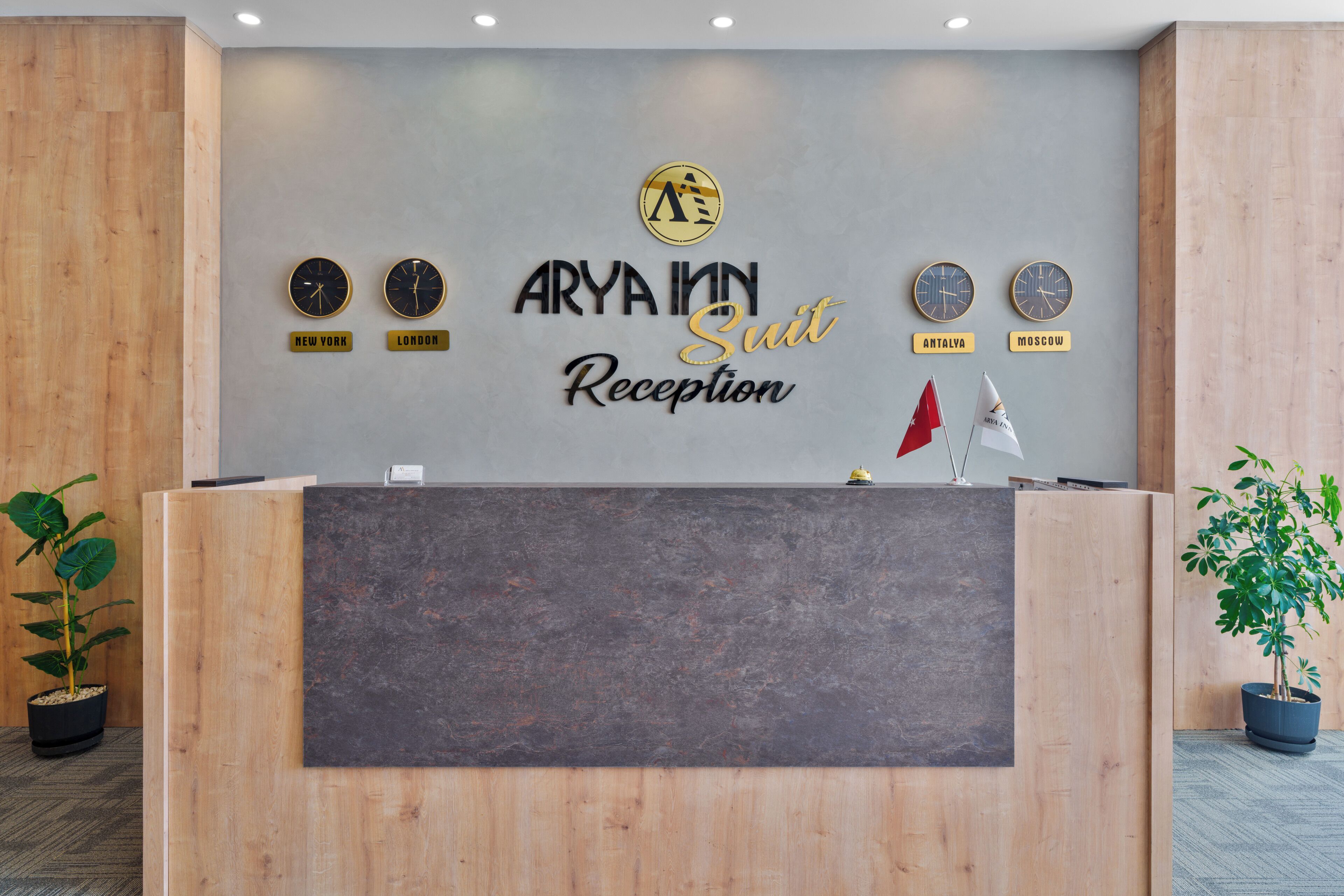A reception desk with a sign reading 'ARYA Inn Suit Reception' and clocks displaying times for New York, London, Antalya, and Moscow.