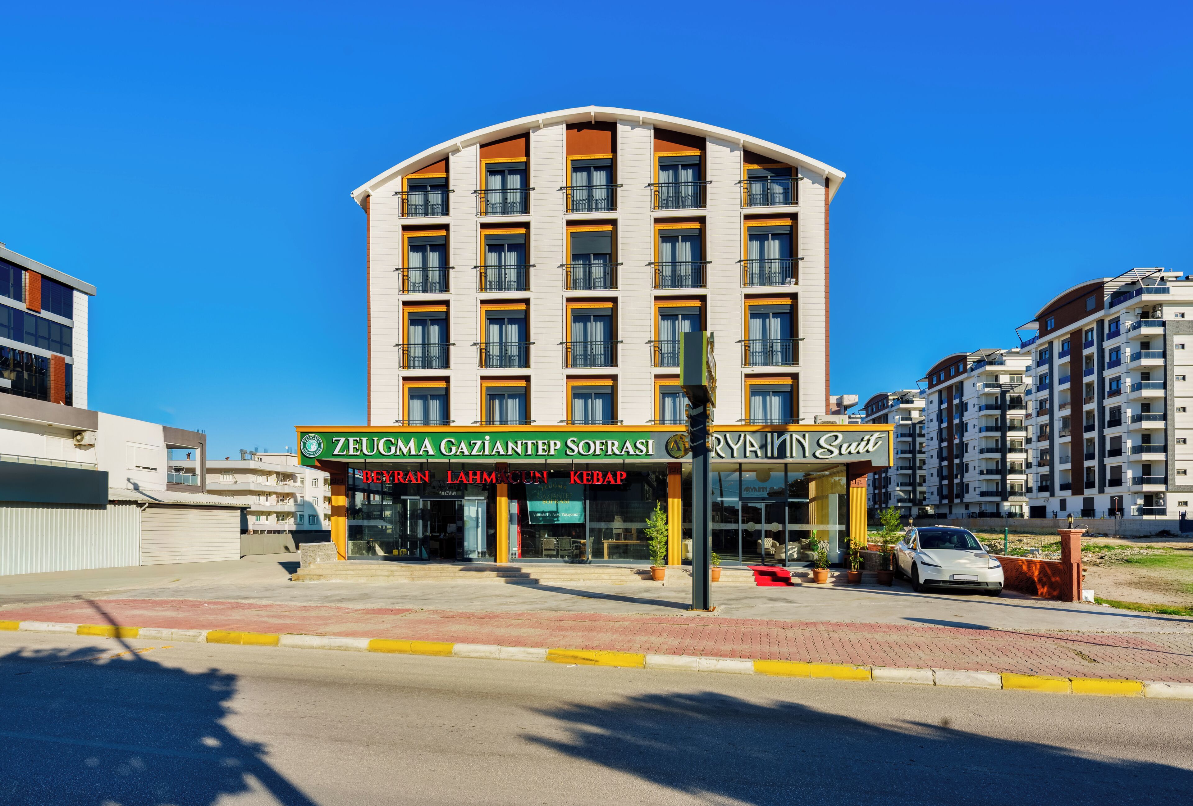A multi-story hotel with a curved facade, featuring a ground-level restaurant and a visible car parked outside.