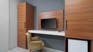 A compact room with a built-in TV, wooden wardrobe, a small desk, and a chair. - ARYA INN SUİT  (Serik)