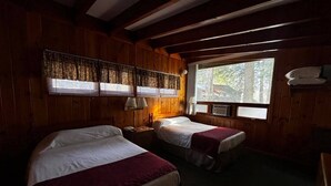 A room with two beds, wooden walls, a window with blinds, and a wall-mounted lamp. - Cozy 1BR hotel room, Hamilton - #348 Iroquois (Hamilton)