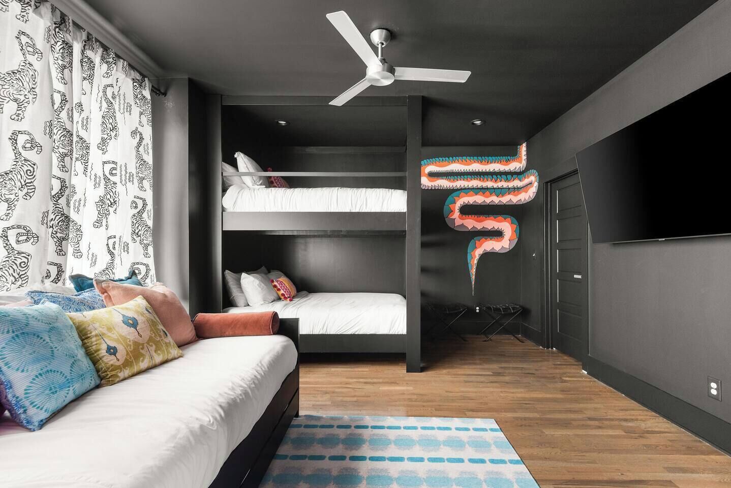 Een slaapkamer met een stapelbed, een plafondventilator, een kamerkleed en een televisie aan de muur.