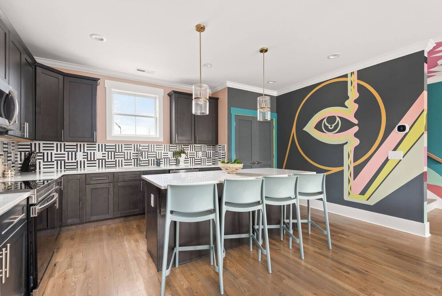 A modern kitchen with dark cabinets, a patterned backsplash, a central island with bar stools, and a large abstract wall mural.