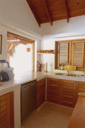 A kitchen with wooden cabinets, a dishwasher, a sink, and a window with blinds. - 2-bedroom apartment in soothing Punta Cana with AC and gym access (Punta Cana)