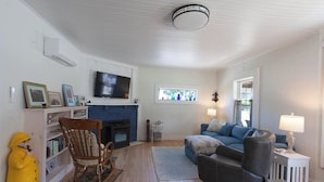 A living room with a fireplace, a television, a sofa, and a chair. - Lock`s Nest on Peaks Island Maine (Portland)
