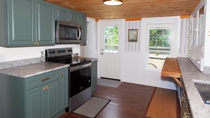 A kitchen with teal cabinets, a microwave, stove, and a wooden ceiling. - Lock`s Nest on Peaks Island Maine (Portland)