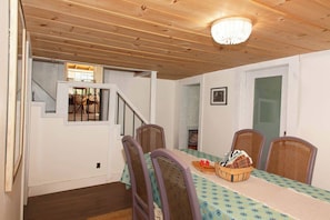 A dining area with a table set for four, surrounded by wicker chairs, a chandelier, and a staircase leading to another room.