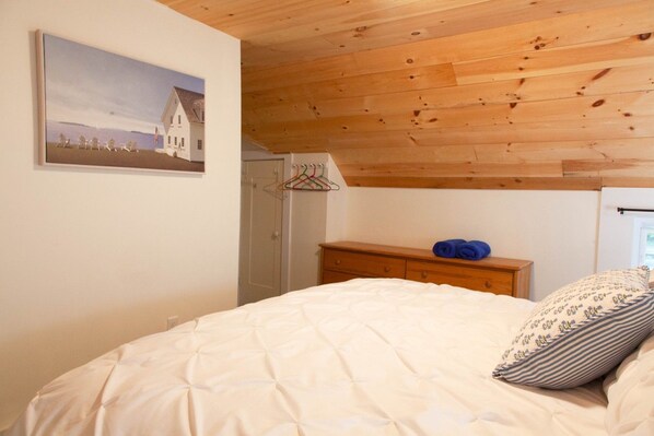 A bedroom with a bed, a wooden dresser, a hanging coat rack, and a painting on the wall.