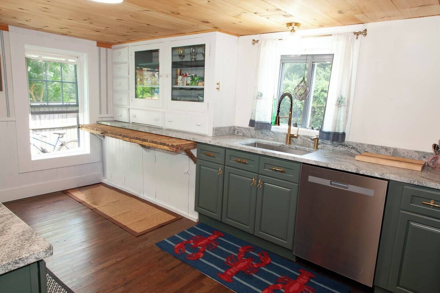 A kitchen with wooden cabinets, a built-in oven, a stainless steel dishwasher, and a window with a view of greenery.