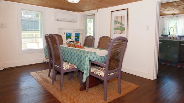 A dining area with a wooden ceiling, a chandelier, a table with a patterned tablecloth, and wicker chairs. - Lock`s Nest on Peaks Island Maine (Portland)