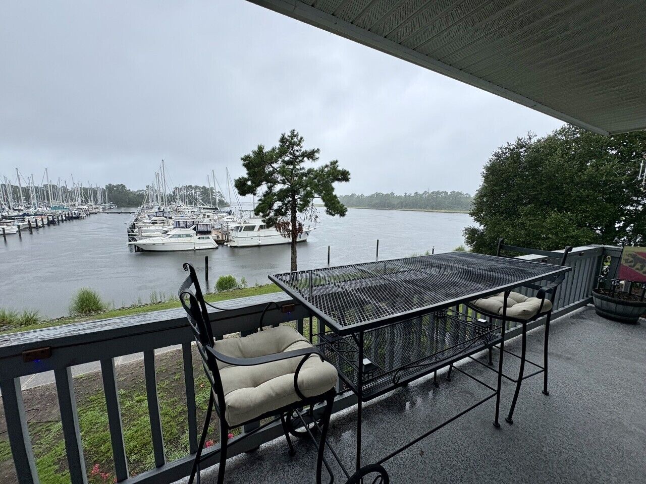 Ein überdachter Außenbereich mit Tisch und Stühlen, mit Blick auf einen Jachthafen und Boote.