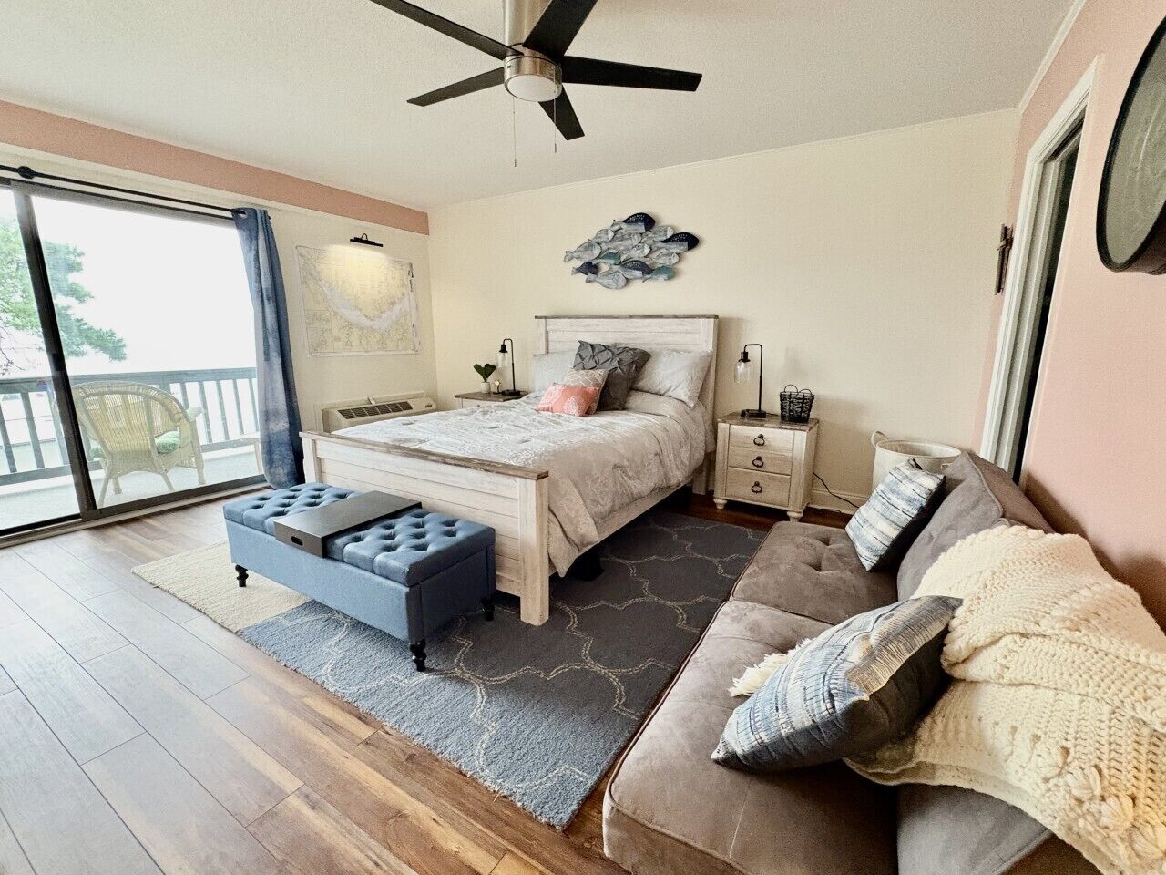 A bedroom with a bed, a sofa, a side table, a nightstand, a ceiling fan, and a view through a sliding door.