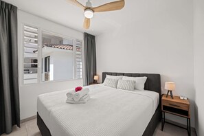 Ein Hotelzimmer mit einem Bett, einem Nachttisch, einer Lampe, einem Deckenventilator und einem Fenster mit Blick nach draußen.