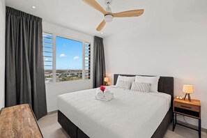 A hotel room with a large bed, two bedside tables with lamps, a ceiling fan, and a window with blinds. - Mirador Azul - Golf Course View Apartment (Blue Bay Golf & Beach Resort)