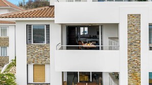 En moderne bygning i to etager med en balkon, et køkken der ses gennem en åben dør, og en facade i sten.